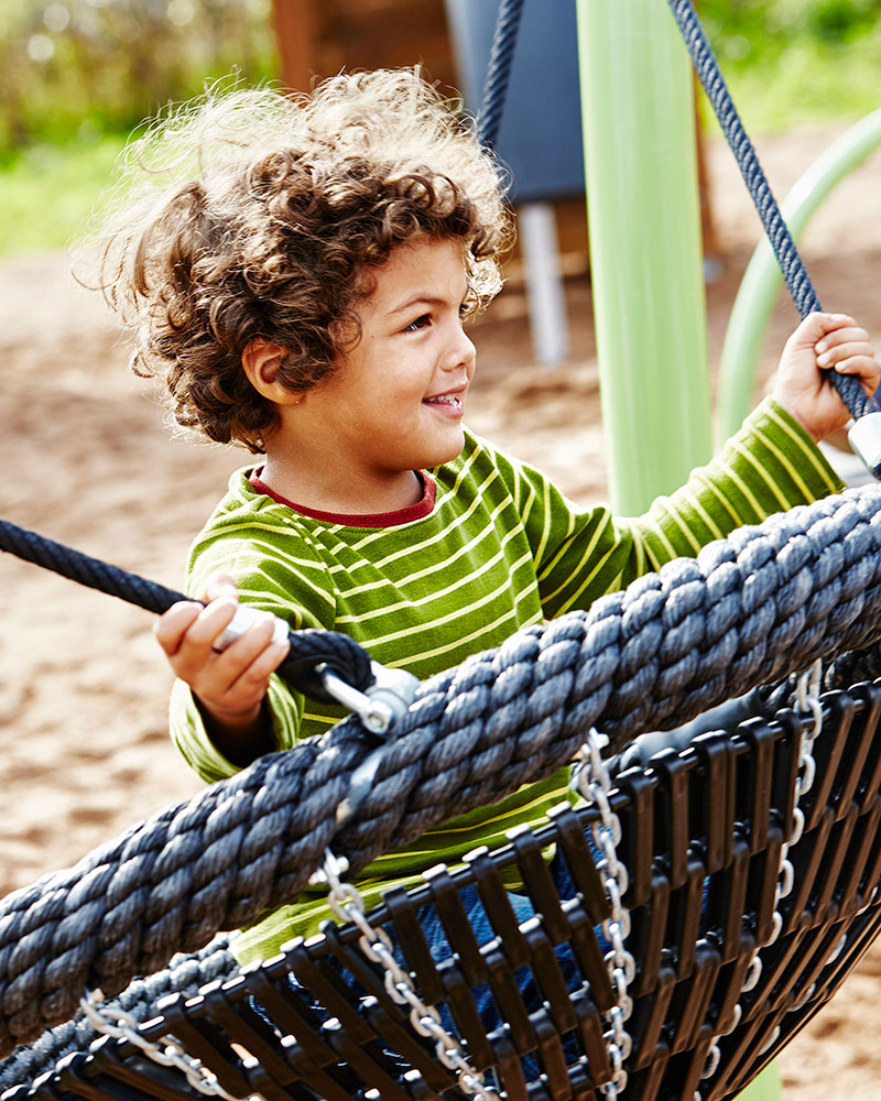 Young boy swining on a basket swing seat.